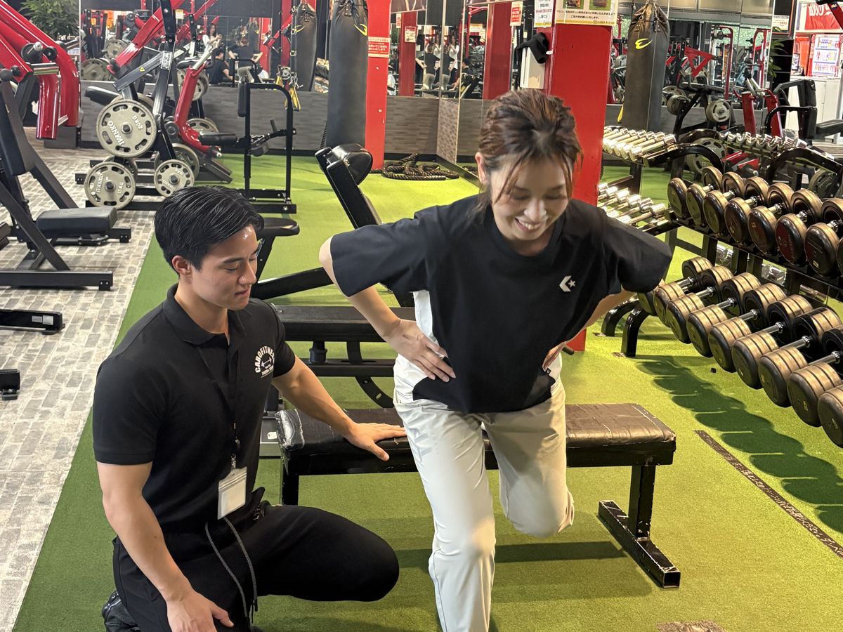 トレーナーが女性の会員さんのフォームを近くで確認しながら指導している様子